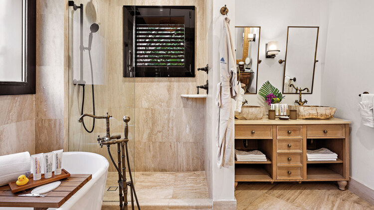 Soaker tub beside glass shower, brown vanity and mirrors
