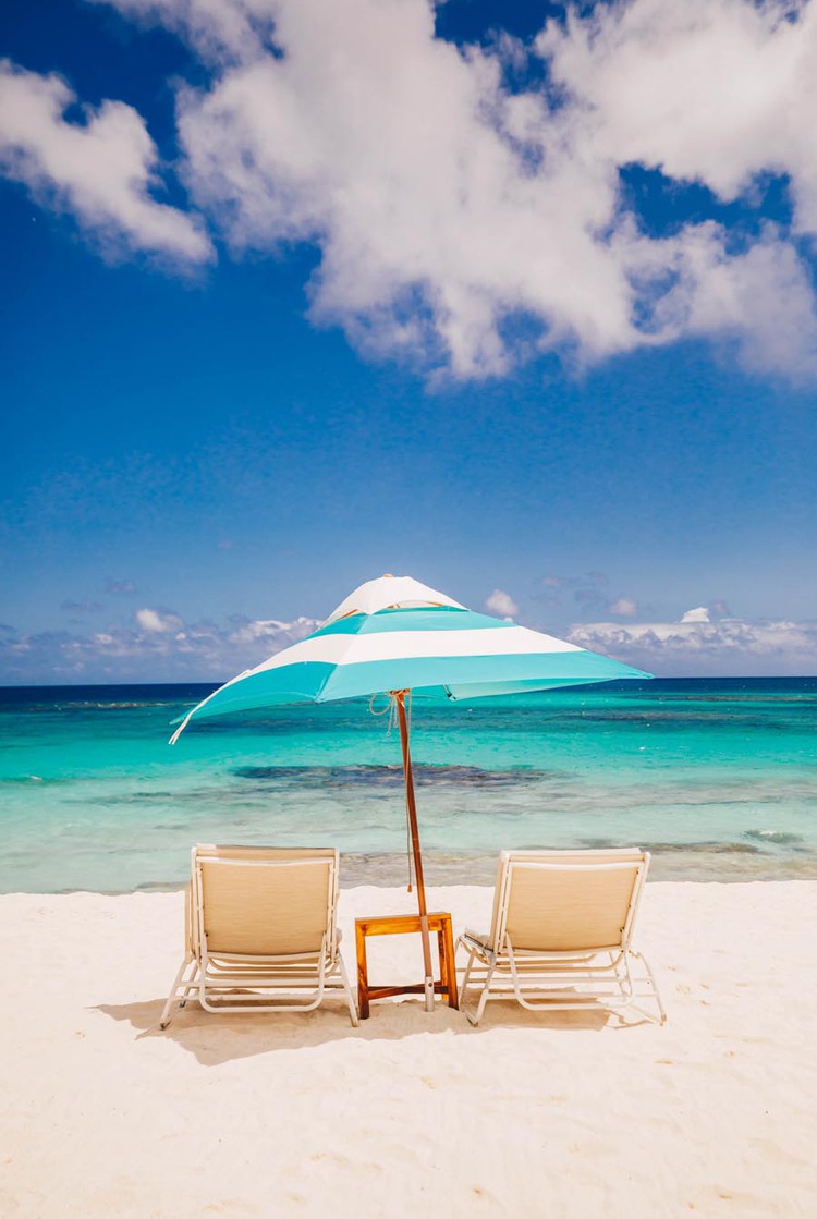 Duas cadeiras de praia com guarda-chuva azul e branco de frente para o mar