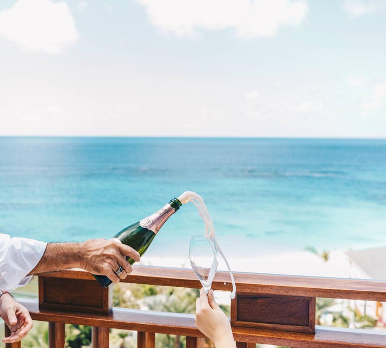 Hombre vertiendo champán en una copa con el océano de fondo