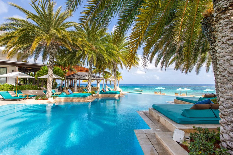 Large pool with lounge chairs surrounded by palm trees and facing the beach