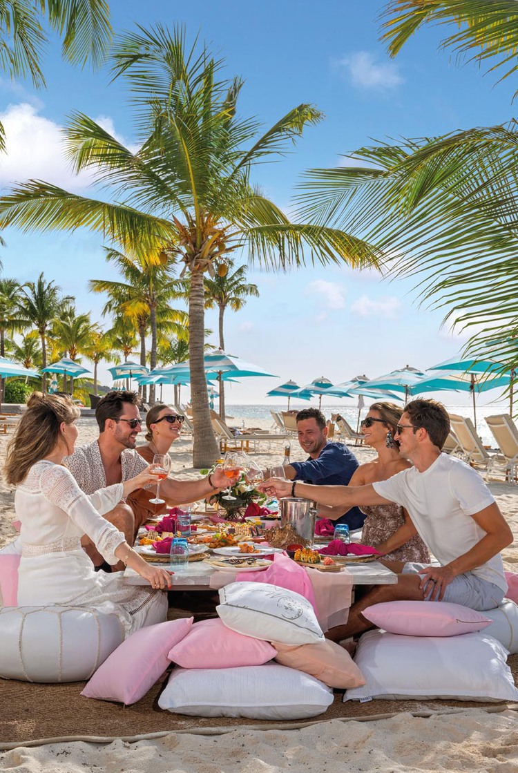Group of people sitting on pillows while having dinner on beach