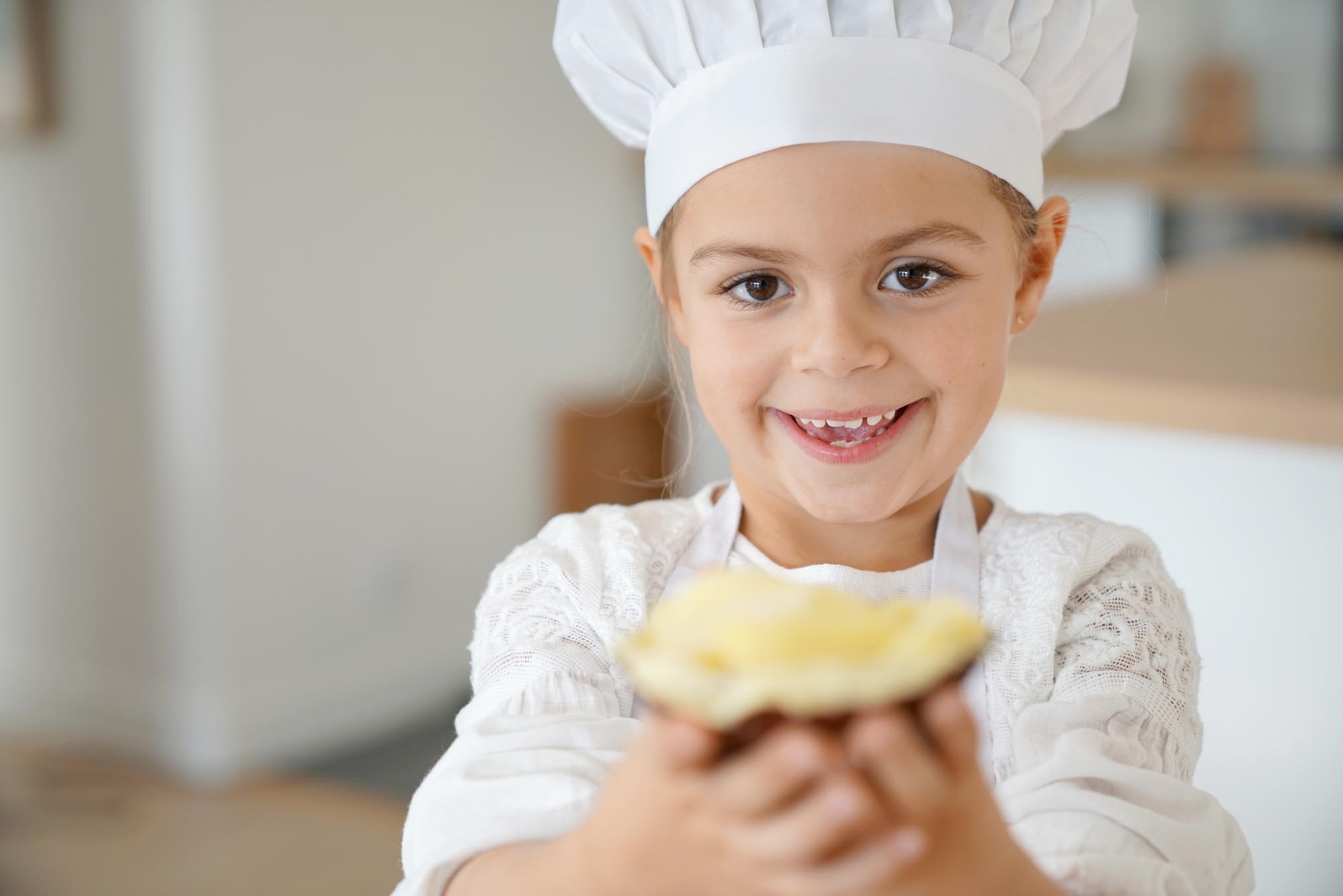 Little girl in chef outfit holding piece of coconut