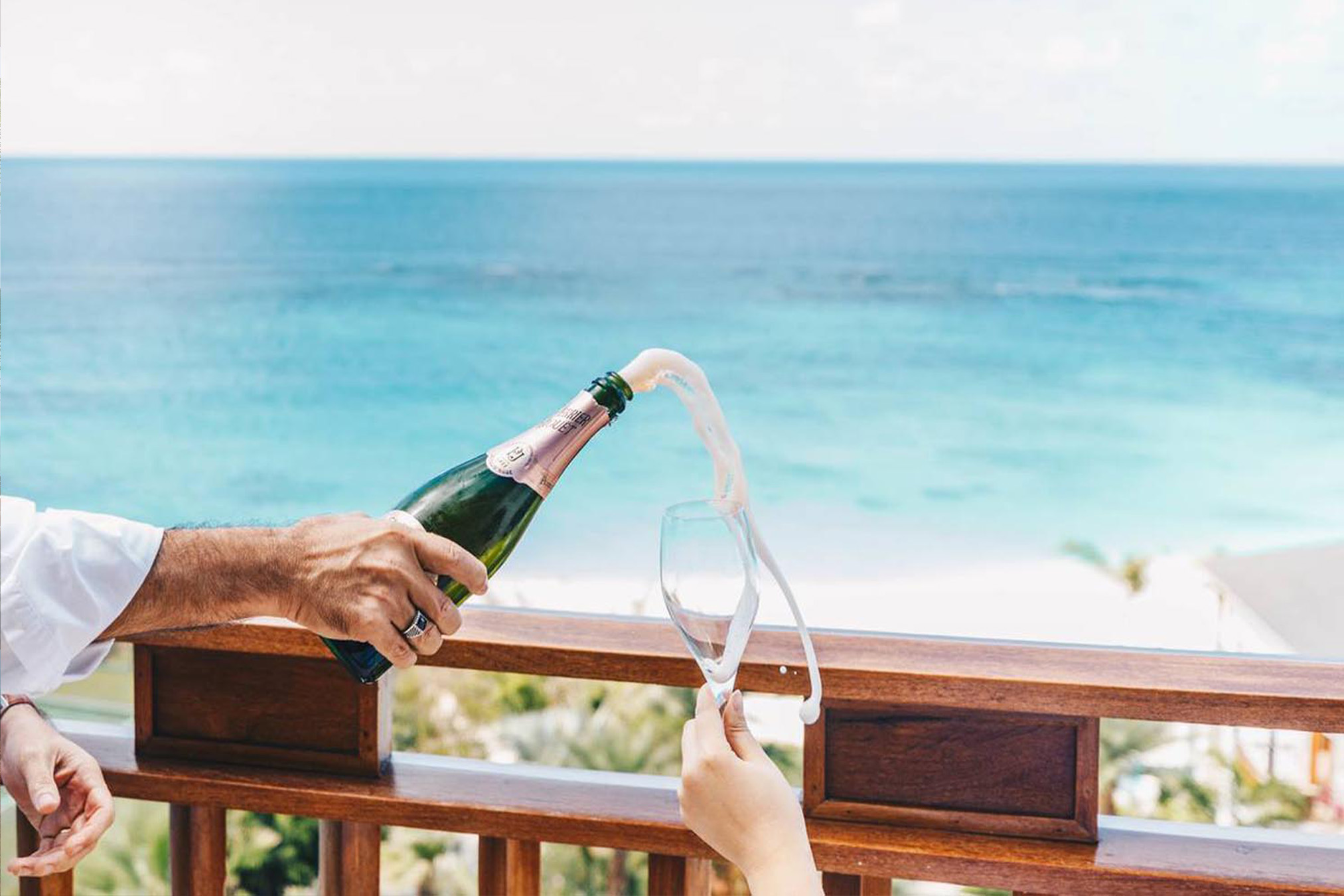 Man pouring champagne into glass with ocean in background