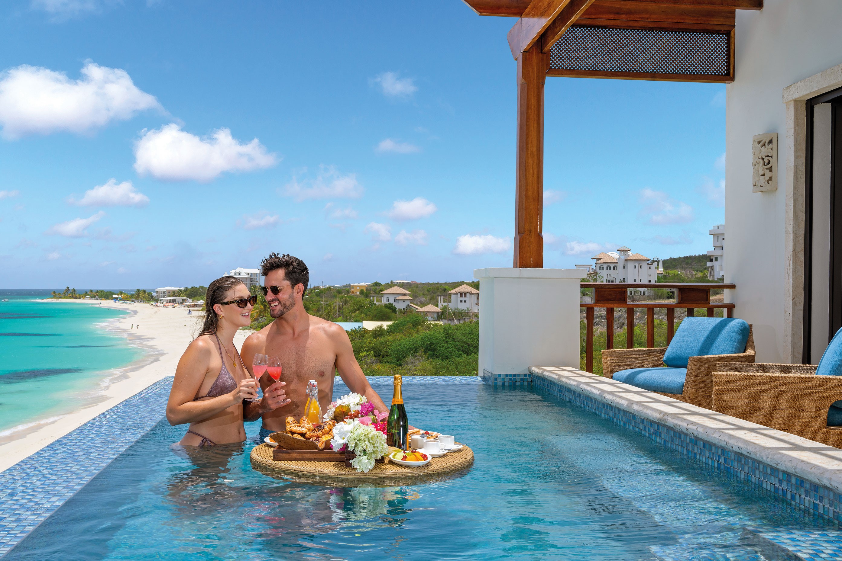 Uomo e donna seduti in piscina con champagne e cibo