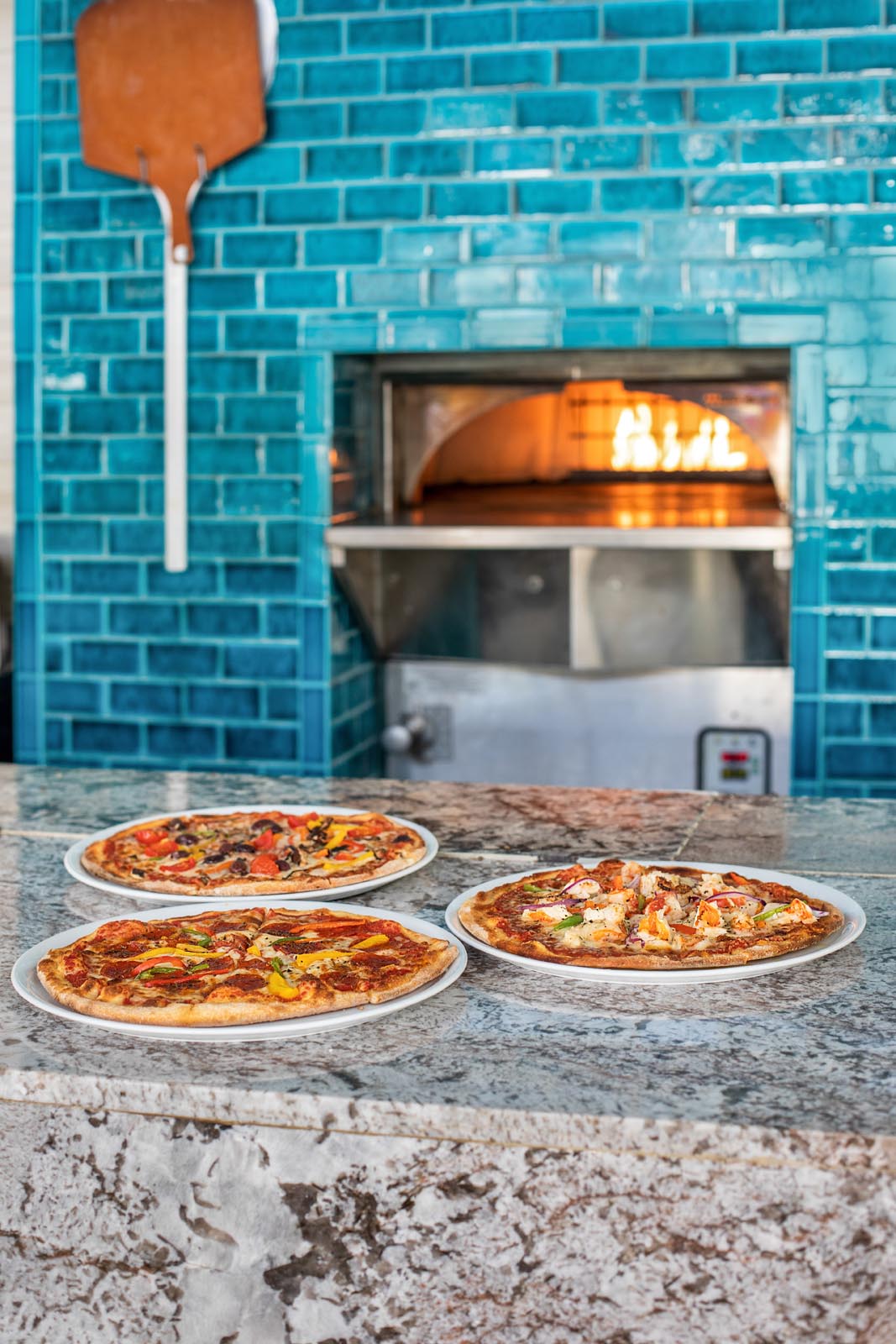 Três pizzas na mesa de mármore ao lado do forno de pizza